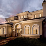 Large stucco home at dusk with arched aluminum windows